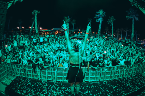 CANDICE raising her arms toward a palm-lined outdoor audience